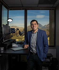 Rick Hernandez smiles in a professional office with a mountain view visible through the window behind him. He wears a blue blazer.