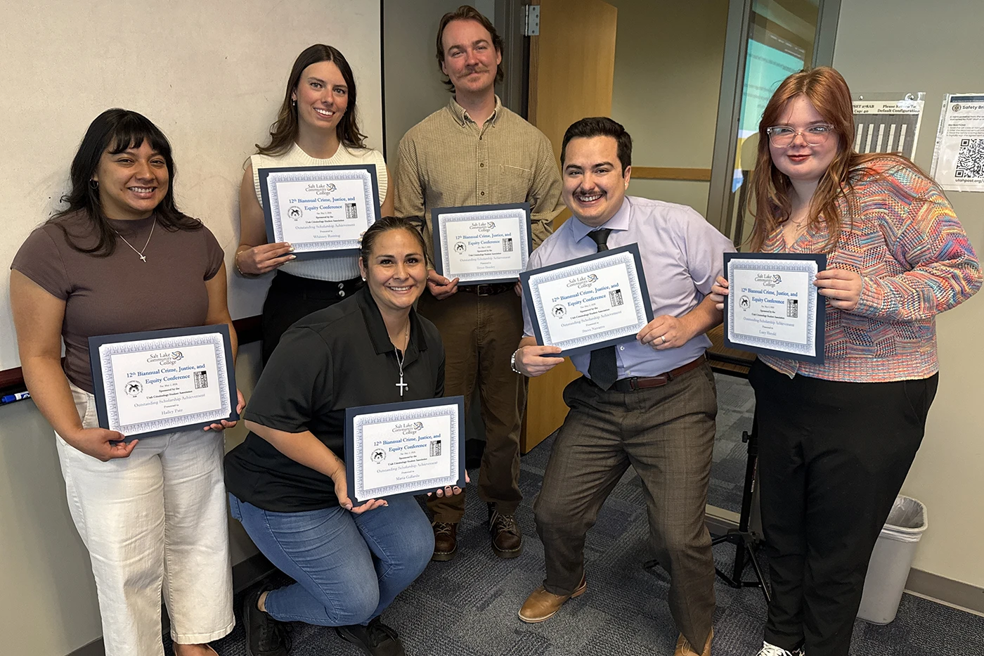 Six people pose together holding framed certificates from the 12th Biannual Crime, Justice, and Equity Conference at Salt Lake Community College, awarded for Outstanding Scholarship Achievement.