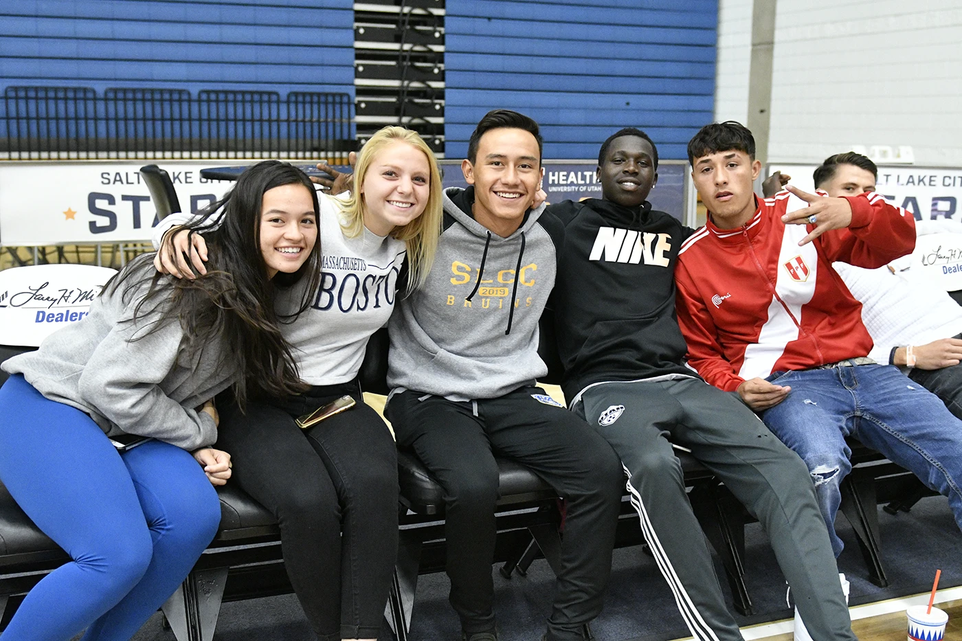 Five students representing different ethnicities are sitting on a bench, smiling at the camera.