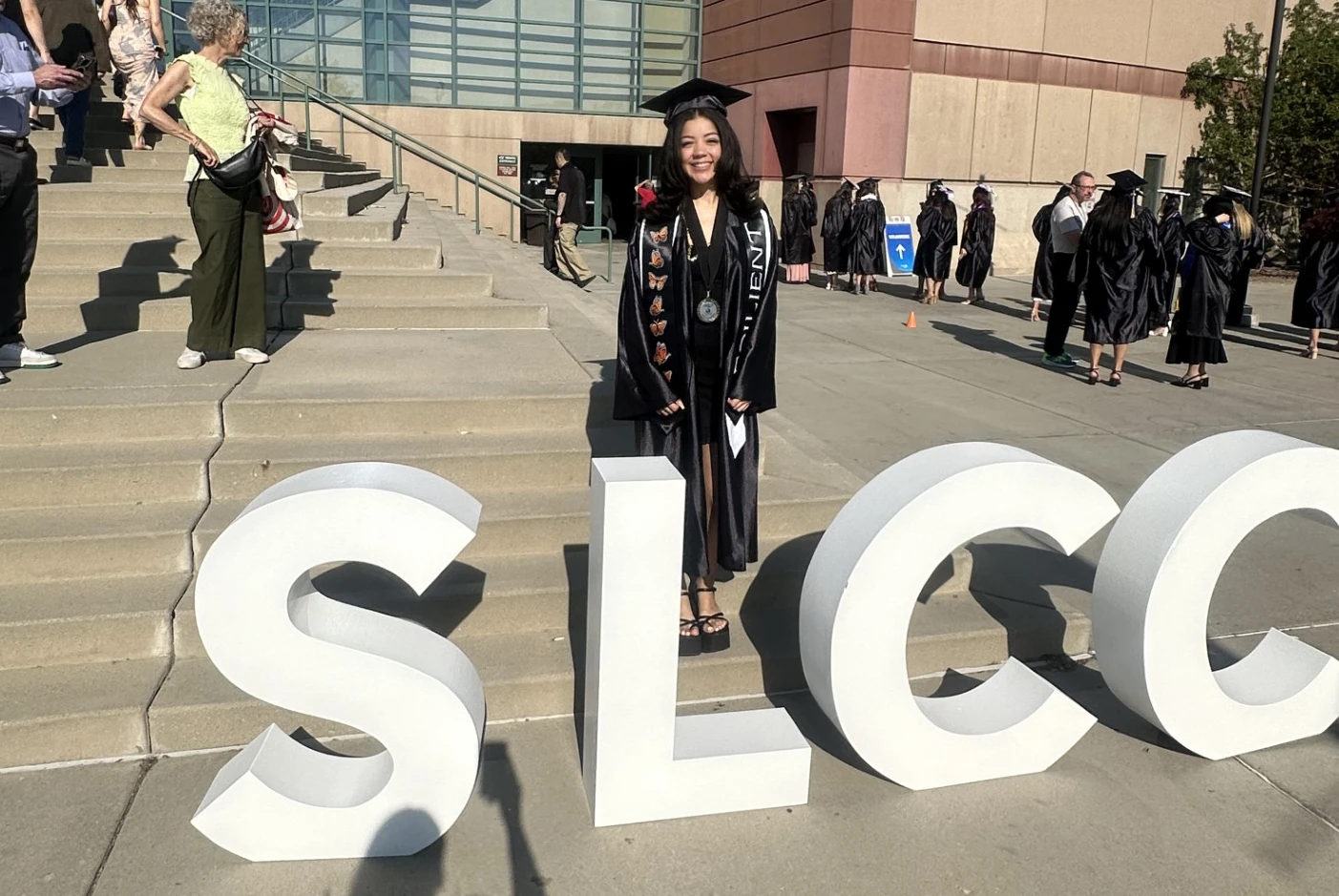 Angelique Wallace in cap and gown, standing behind SLCC block letters.