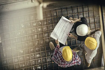 three people with hardhats looking at blueprints